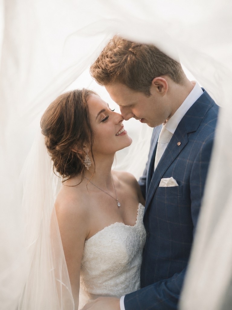 Alex and Julia smiling under the veil